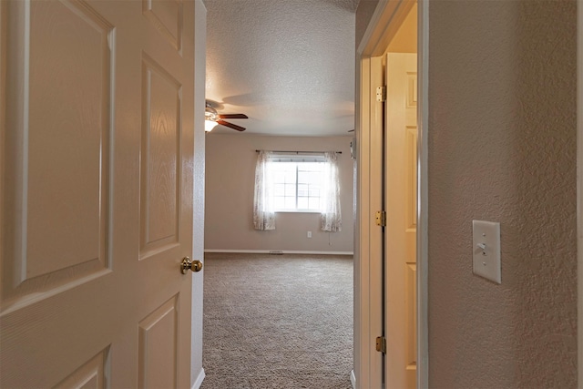 corridor with baseboards, carpet floors, a textured ceiling, and a textured wall