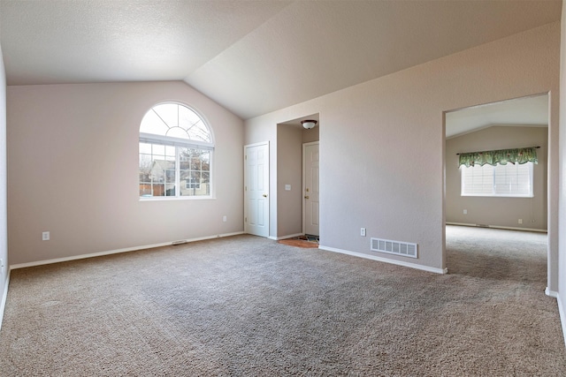 carpeted empty room featuring visible vents, a healthy amount of sunlight, baseboards, and vaulted ceiling