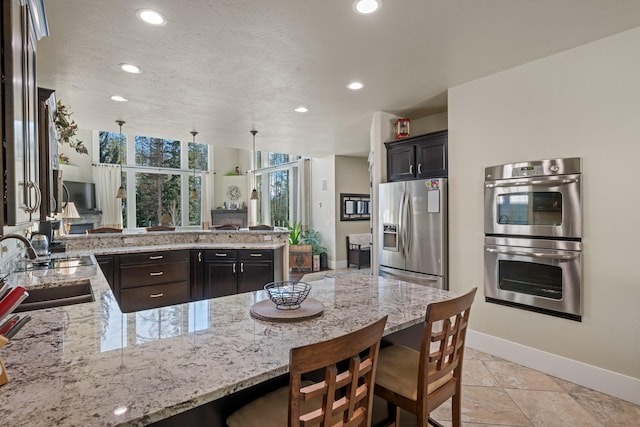 kitchen featuring light stone counters, stainless steel appliances, a peninsula, and a breakfast bar