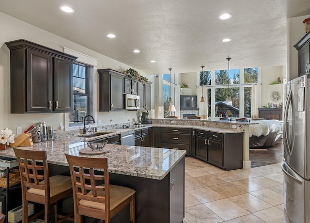 kitchen featuring a sink, dark brown cabinetry, appliances with stainless steel finishes, a peninsula, and light stone countertops