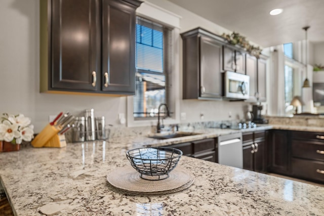 kitchen with white microwave, dark brown cabinetry, light stone countertops, and a sink