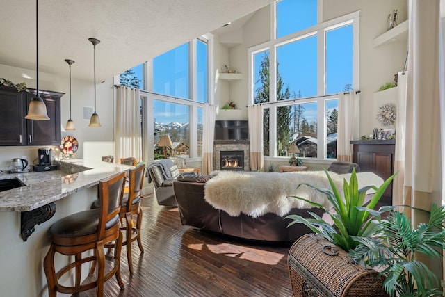 living room with a high ceiling, dark wood-style floors, a fireplace, and a textured ceiling