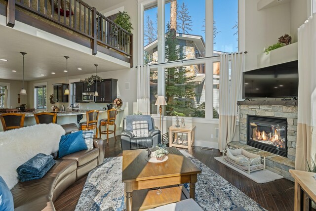 living area featuring a stone fireplace, dark wood-type flooring, baseboards, and a towering ceiling