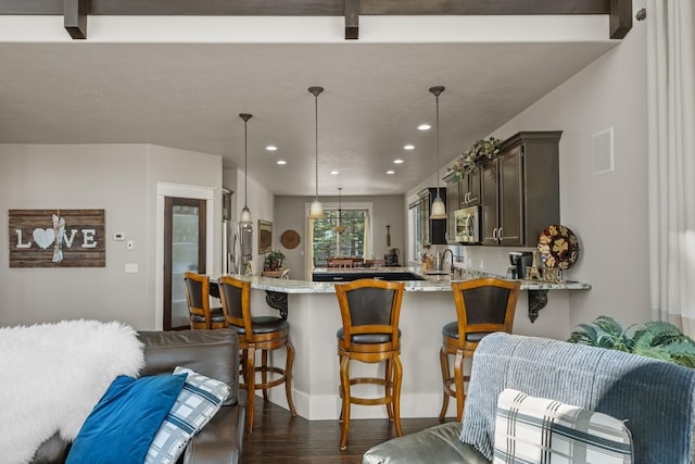 kitchen with light stone counters, a peninsula, recessed lighting, dark wood-type flooring, and stainless steel microwave