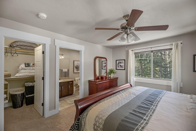 bedroom featuring ceiling fan, a spacious closet, a closet, ensuite bathroom, and light carpet