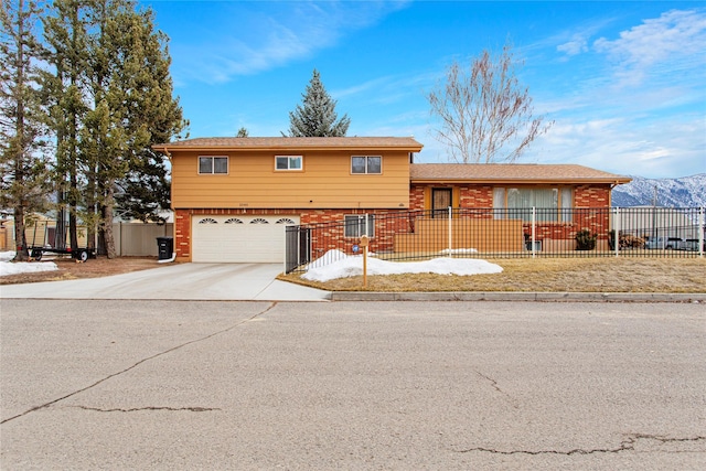 tri-level home featuring brick siding, an attached garage, concrete driveway, and fence