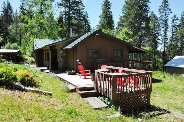 rear view of house featuring stone siding, a lawn, metal roof, and a deck