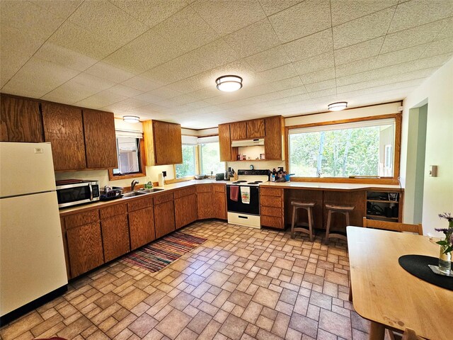 kitchen with brown cabinetry, freestanding refrigerator, electric stove, under cabinet range hood, and stainless steel microwave