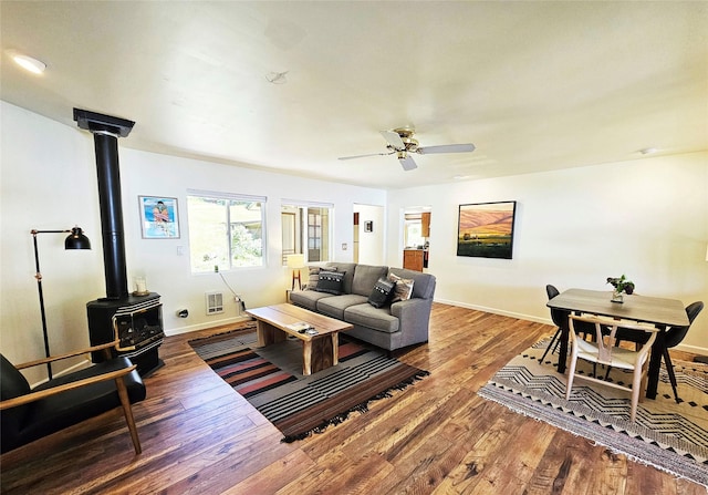 living room with baseboards, a wood stove, ceiling fan, and wood finished floors