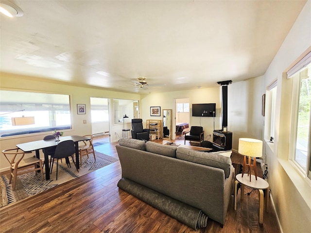 living room with dark wood-type flooring, a wood stove, baseboards, and ceiling fan