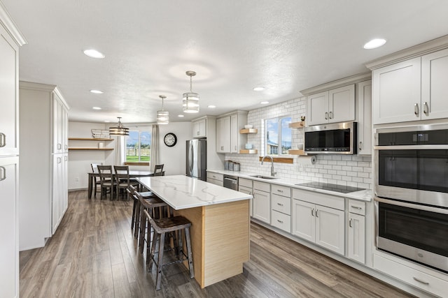 kitchen featuring wood finished floors, open shelves, a sink, appliances with stainless steel finishes, and backsplash