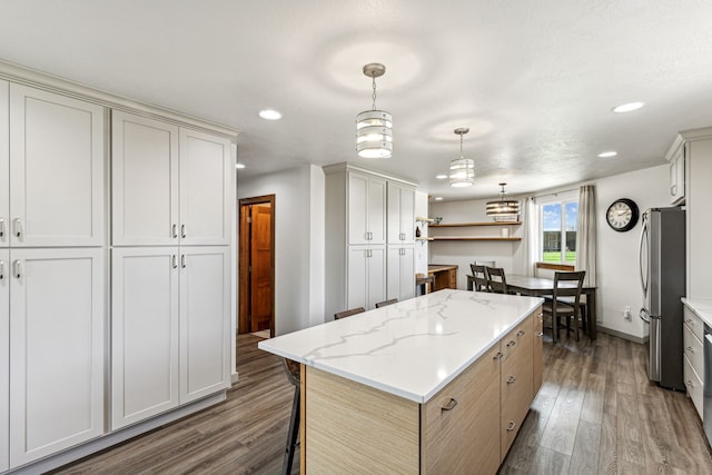 kitchen featuring pendant lighting, wood finished floors, a center island, freestanding refrigerator, and light stone countertops