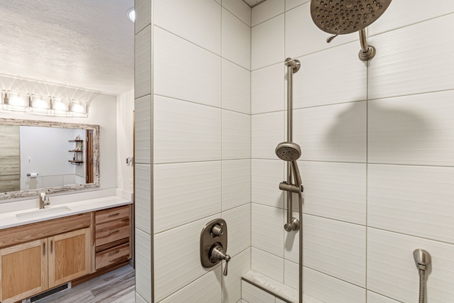 full bathroom featuring a tile shower, a textured ceiling, vanity, and wood finished floors