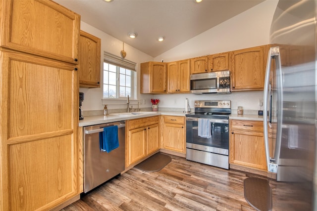 kitchen with lofted ceiling, a sink, light countertops, light wood-style floors, and appliances with stainless steel finishes