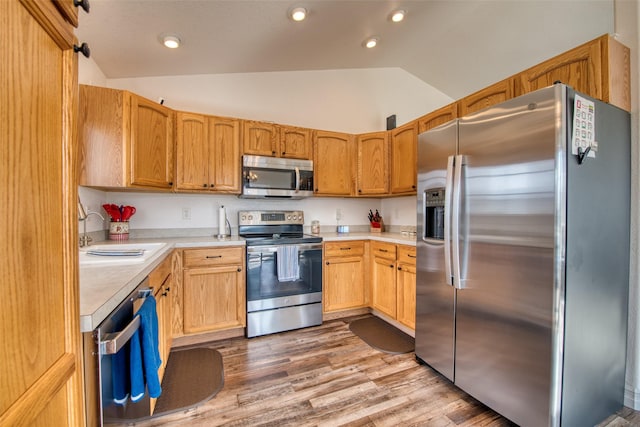 kitchen featuring lofted ceiling, a sink, stainless steel appliances, light countertops, and light wood-style floors