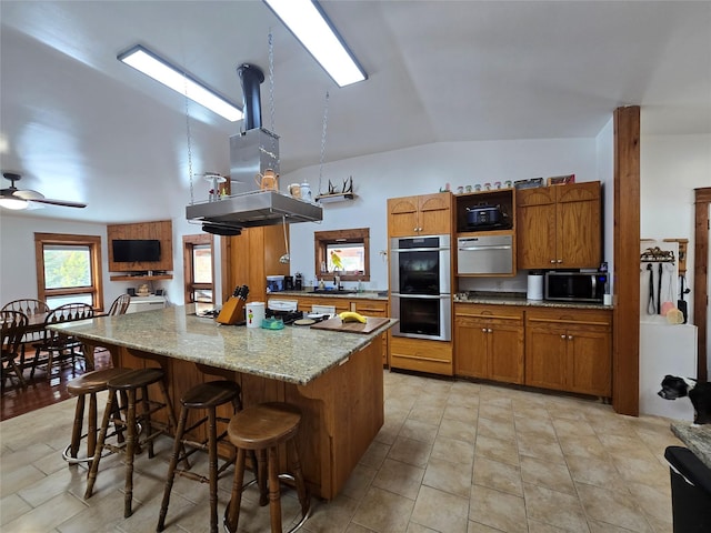 611 S Canyon Dr, Seeley Lake, MT 59868 - kitchen with stainless steel appliances, brown cabinets, lofted ceiling, a breakfast bar area, and a center island