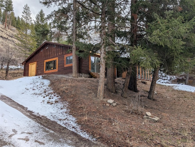 view of snow covered exterior with log siding and board and batten siding