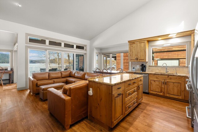 kitchen with high vaulted ceiling, a sink, dishwasher, light wood-style flooring, and light stone countertops