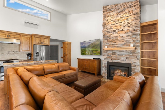 living area with a stone fireplace, an AC wall unit, a towering ceiling, and wood finished floors