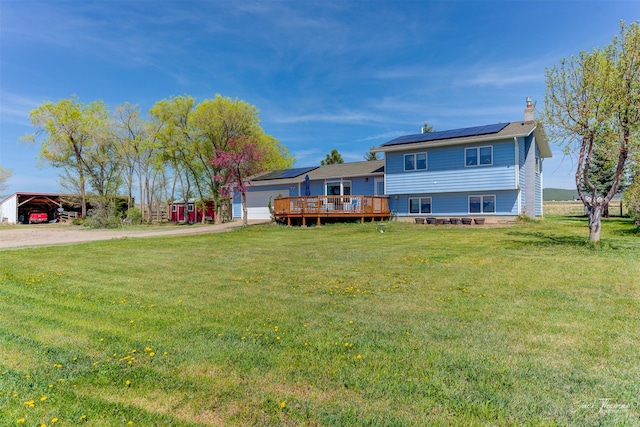 rear view of property featuring driveway, solar panels, a chimney, and a lawn