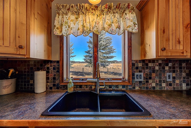 kitchen with dark countertops, a sink, decorative backsplash, and brown cabinetry
