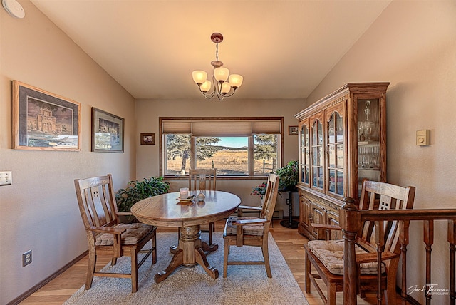 dining space featuring light wood finished floors, a chandelier, lofted ceiling, and baseboards