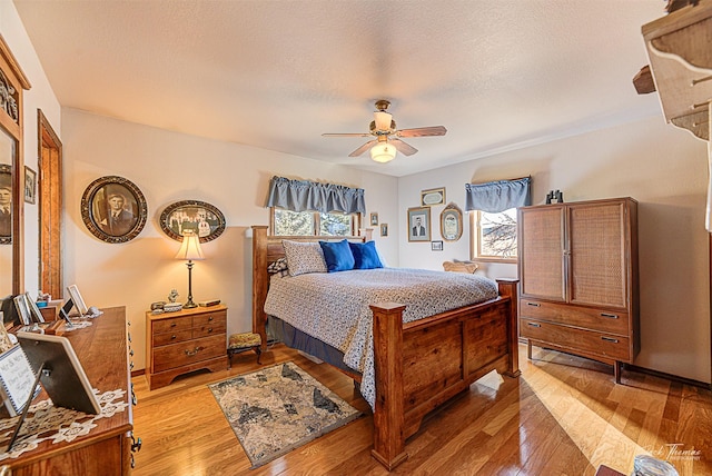 bedroom featuring multiple windows, light wood finished floors, a ceiling fan, and a textured ceiling