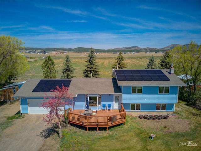 view of front of property with driveway, solar panels, a deck with mountain view, a garage, and roof with shingles