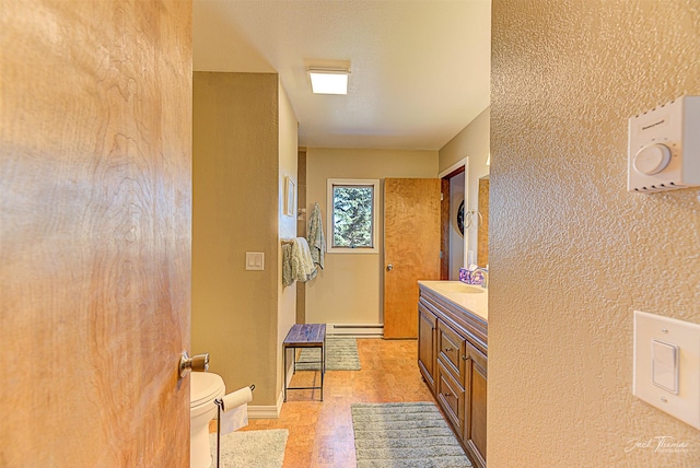 bathroom with a baseboard heating unit, toilet, vanity, baseboards, and a textured wall
