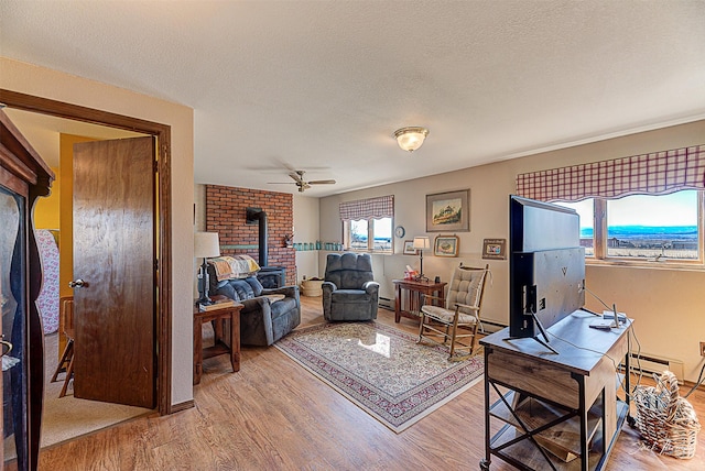 living area featuring a wood stove, wood finished floors, ceiling fan, a textured ceiling, and a baseboard radiator