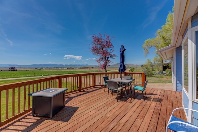deck featuring outdoor dining space, a rural view, and a lawn