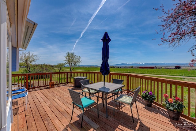 wooden terrace with outdoor dining area, a view of rural / pastoral area, and a yard
