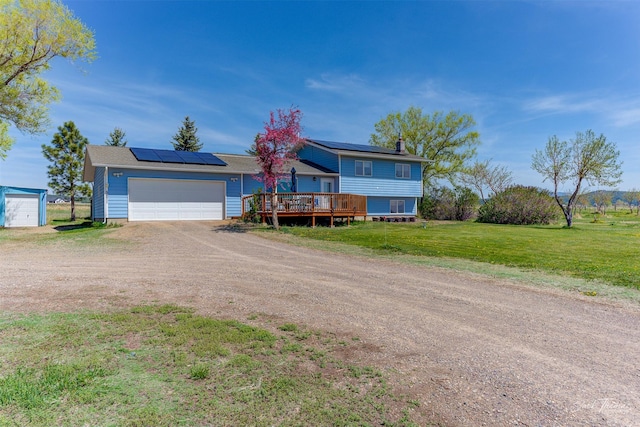 view of front of property featuring driveway, a deck, roof mounted solar panels, a front yard, and a chimney