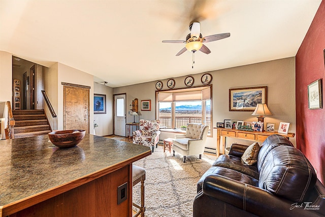 living area featuring baseboard heating, ceiling fan, and stairs