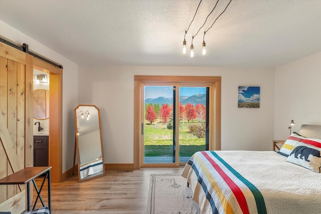 140 Swan River Rd, Bigfork, MT 59911 - bedroom with access to outside, light wood finished floors, a barn door, rail lighting, and connected bathroom