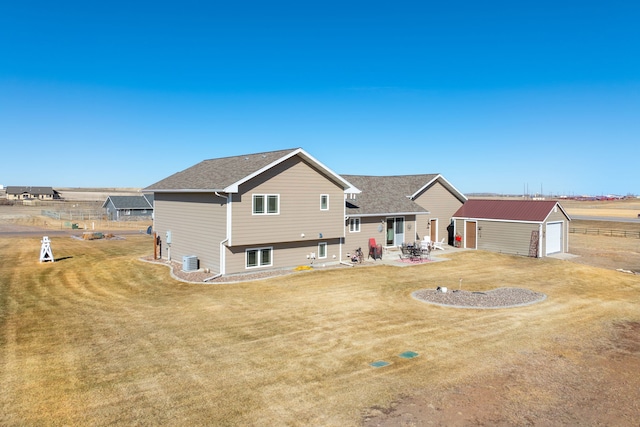 rear view of property featuring a shingled roof, central air condition unit, a lawn, an outdoor structure, and a patio