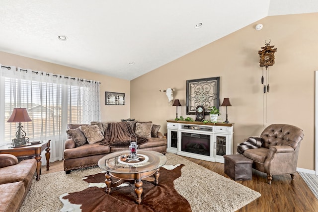 living room with lofted ceiling, a glass covered fireplace, wood finished floors, recessed lighting, and baseboards