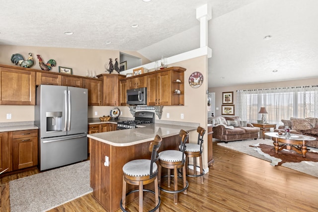kitchen featuring open floor plan, lofted ceiling, light wood-style flooring, brown cabinetry, and stainless steel appliances