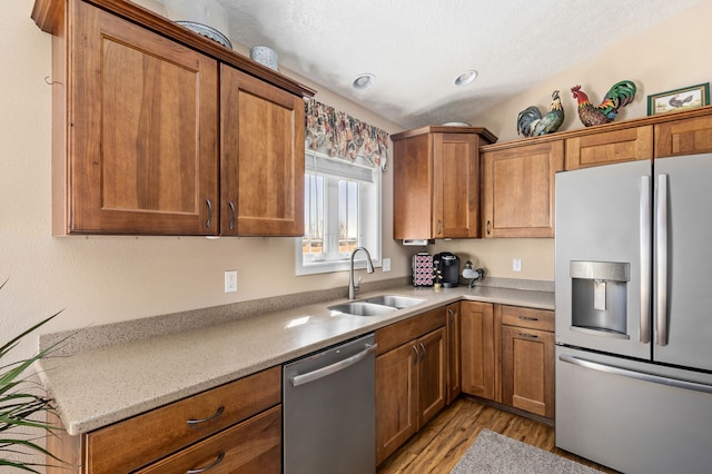 kitchen with a sink, light wood-style floors, appliances with stainless steel finishes, brown cabinetry, and light countertops