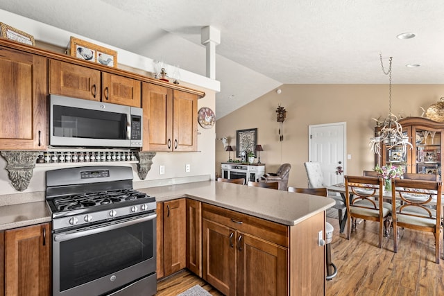 kitchen with vaulted ceiling, light wood-style flooring, a peninsula, brown cabinets, and stainless steel appliances