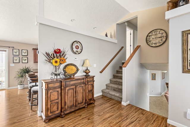 stairs with baseboards, a textured ceiling, lofted ceiling, and wood finished floors