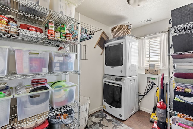 clothes washing area with visible vents, laundry area, stacked washer and clothes dryer, a textured ceiling, and tile patterned floors