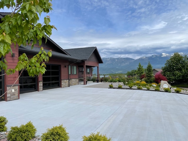 113 Mission Bay Dr, Polson, MT 59860 - view of property exterior featuring a mountain view, stone siding, a garage, a porch, and concrete driveway