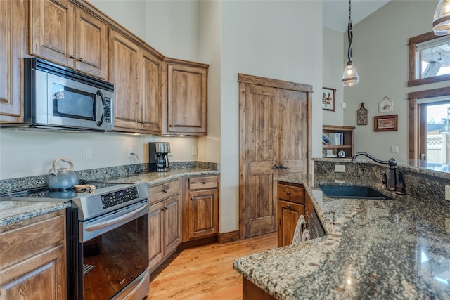 1 Rock Creek Ct, Whitefish, MT 59937 - kitchen featuring appliances with stainless steel finishes, a towering ceiling, brown cabinetry, light wood-style floors, and hanging light fixtures