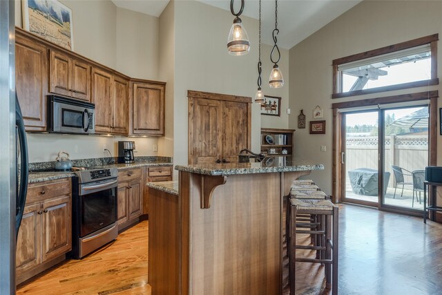 1 Rock Creek Ct, Whitefish, MT 59937 - kitchen with stainless steel appliances, high vaulted ceiling, a breakfast bar, brown cabinetry, and stone countertops