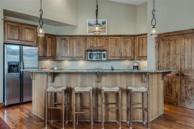 1 Rock Creek Ct, Whitefish, MT 59937 - kitchen with stainless steel appliances, light stone counters, dark wood-style flooring, a breakfast bar area, and a towering ceiling