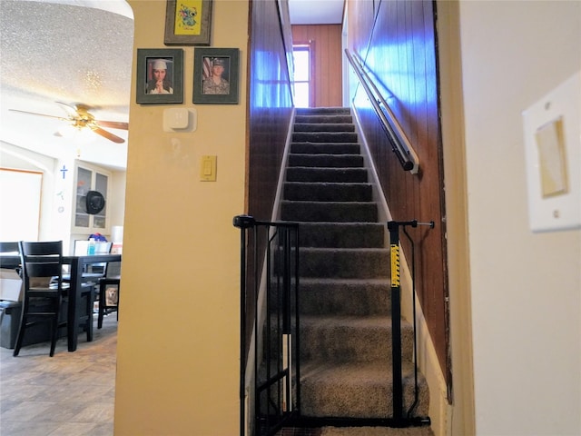 stairway with a textured ceiling and a ceiling fan