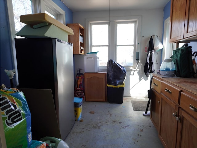 kitchen with brown cabinets, unfinished concrete flooring, light countertops, and freestanding refrigerator