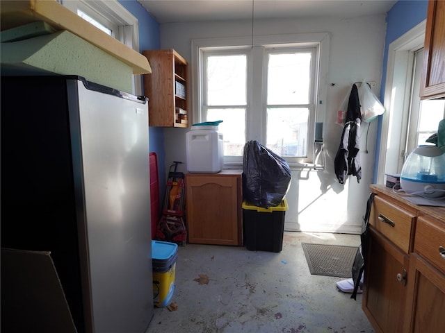 kitchen with concrete flooring, brown cabinets, and freestanding refrigerator