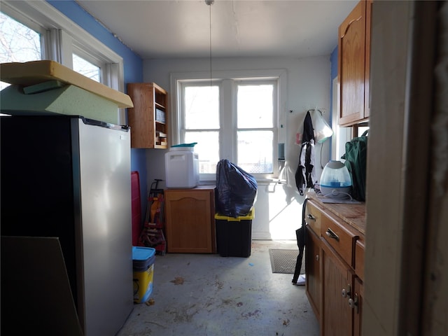 kitchen featuring unfinished concrete flooring, brown cabinets, a healthy amount of sunlight, and freestanding refrigerator
